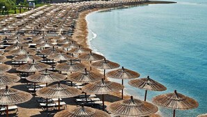 A beach with numerous thatched umbrellas and sun loungers arranged in rows along the shoreline.