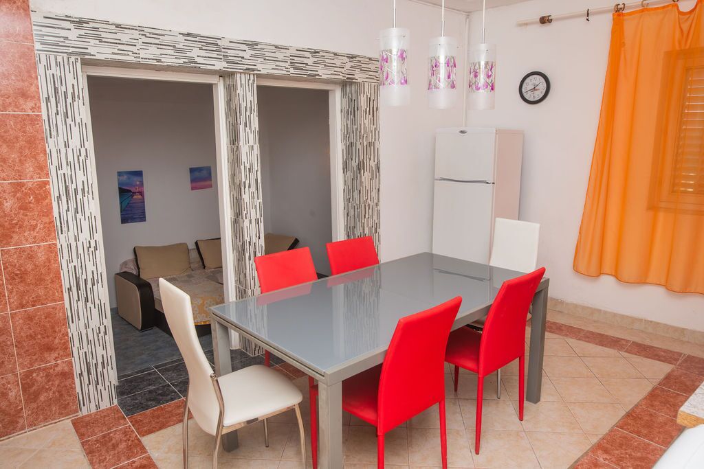 Un coin repas avec une table en verre, des chaises rouges, un canapé blanc et un réfrigérateur.