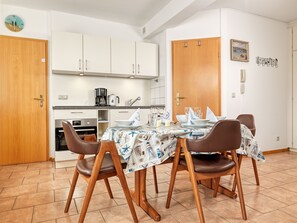 A compact kitchen with modern appliances, a dining area with a table set for four, and a wooden door.