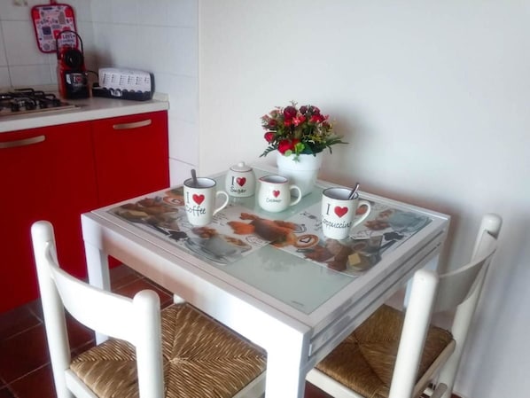Een kleine eettafel met vier koffiemokken, een witte vaas met bloemen en een rode kast op de achtergrond.