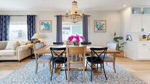 A modern living room with a dining area, featuring a chandelier, patterned rug, and artwork on the walls. - Shared Pool, Boardwalk to Beach and Golf Cart Included (Port Aransas)