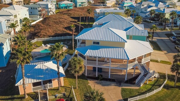 A coastal residential area with houses featuring blue roofs and white exteriors, a central house with a balcony, and a clear view of the ocean. - Shared Pool, Boardwalk to Beach and Golf Cart Included (Port Aransas)
