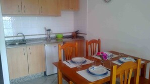 Cozinha compacta com pia, um pequeno frigorífico e armários de madeira. Há uma mesa de jantar posta com pratos, copos e um vaso com flores.