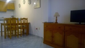 Uma área de refeições com cadeiras de madeira e uma mesa, um armário de madeira com uma televisão e um relógio de parede.