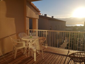 Un balcón con una mesa y sillas, vista al mar y un edificio al fondo.