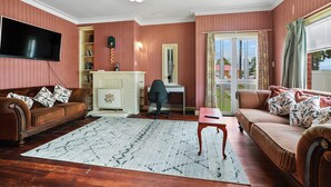 A living room with a sofa, a desk, a TV, and a fireplace. - A cozy art deco farmhouse within walking distances to all amenities in town. (Te Awamutu)