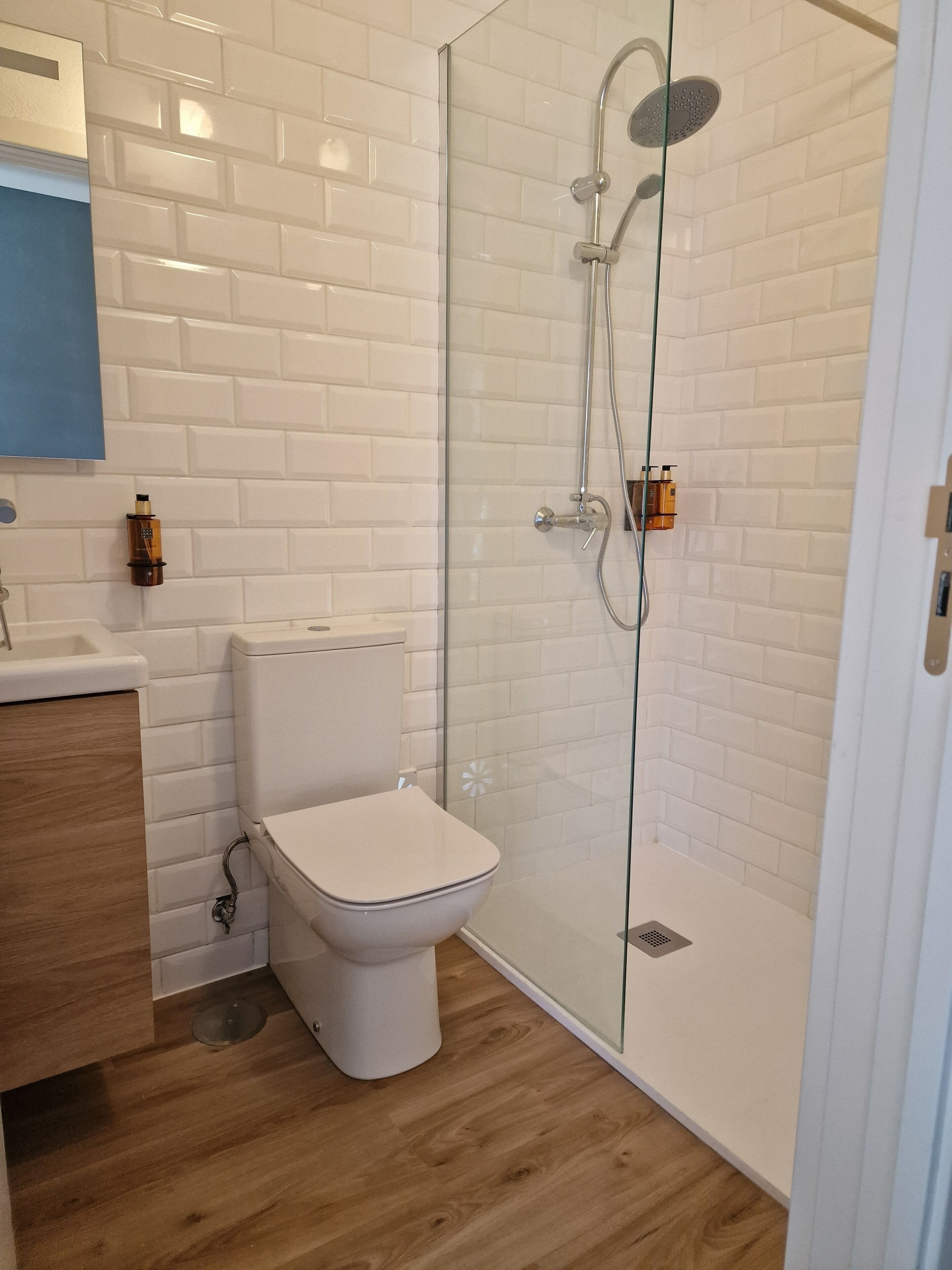 A modern bathroom with a glass-enclosed shower, white subway tiles, and a wooden vanity.