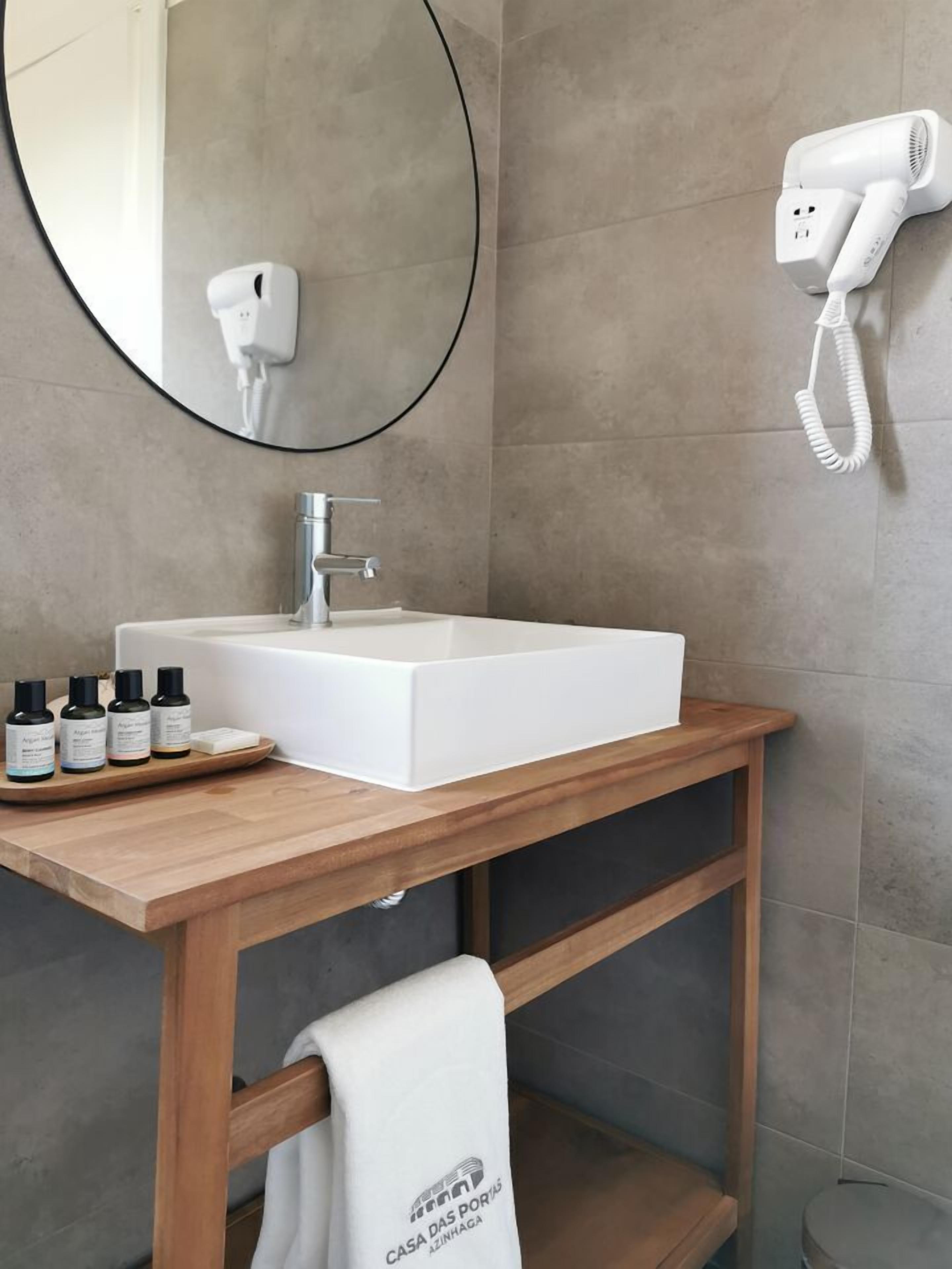 A bathroom with a white sink, a round mirror, a hairdryer, and a towel rack.