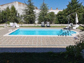 Piscina retangular com deck revestido, cercada por espreguiçadeiras e um gramado.