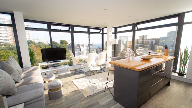 Een moderne woonkamer met een grote televisie, comfortabele zithoek, een keukeneiland en grote ramen met uitzicht over de stad.