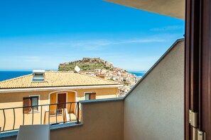 Ein Balkon mit Blick auf eine Küstenstadt, ein markanter Hügel mit einer Festung und das Meer im Hintergrund.