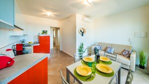 A modern apartment with a kitchen, dining area, and living room. It features a kitchen with a red appliance, a dining table set with yellow plates, and a living room with a beige sofa.