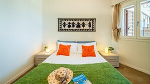 A neatly made bed with a green blanket, two orange pillows, and a decorative wall hanging.