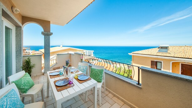 A balcony with a table set for dining, overlooking the sea.