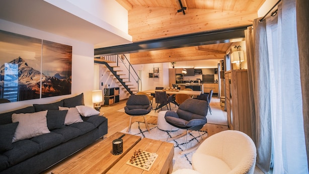 Ein modernes Wohnzimmer mit Holzboden, einer Couch, Sesseln, einem Couchtisch und einem Gemälde von Bergen.