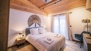 Ein Schlafzimmer mit Oberlichter, einem Bett mit Kissen, einem Nachttisch mit Lampe, einem Sessel und einem Schreibtisch.