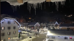 Eine verschneite Straße bei Nacht mit Gebäuden an beiden Seiten, beleuchtet von Straßenlaternen und Weihnachtsdekorationen.
