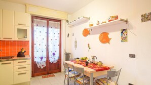 A kitchen with a dining table, chairs, and a window with curtains. There are cabinets, a sink, and a radiator. - Pet friendly apartment in Follonica with WiFi (Follonica)