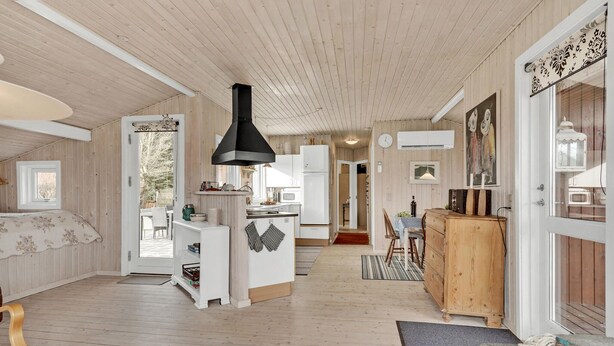 A spacious room with wooden floors, a large black stove, a white refrigerator, and a wooden cabinet. - 3 bedroom stunning home in Juelsminde (Juelsminde)