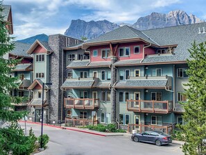 Un hotel de varios pisos con balcones, fachada de piedra y vistas a las montañas.