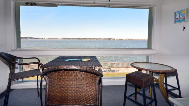 Una habitación con un ventanal grande con vistas a una masa de agua, muebles de mimbre y una pequeña mesa.