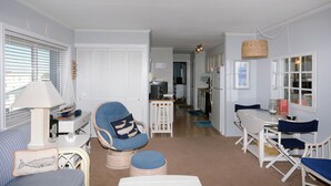 A spacious living room with a sofa, a dining table, and a chair. There is a lamp and a small table with decorative items.