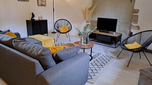 A living room with a grey sofa, two black chairs, a wooden coffee table, a TV on a wooden stand, and a floor lamp. - La Chaumière de Chabine (OIZON)
