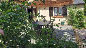 A house with a thatched roof, a window with wooden shutters, and a garden with various plants. - La Chaumière de Chabine (OIZON)