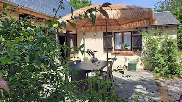 Een huis met rieten dak, een raam met houten luiken en een tuin met verschillende planten.