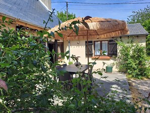 A house with a thatched roof, a window with wooden shutters, and a garden with various plants.