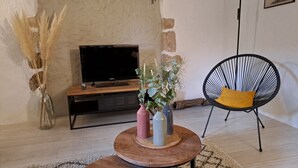 A living room with a TV, a round wooden coffee table, a chair, and two vases with plants. - La Chaumière de Chabine (OIZON)