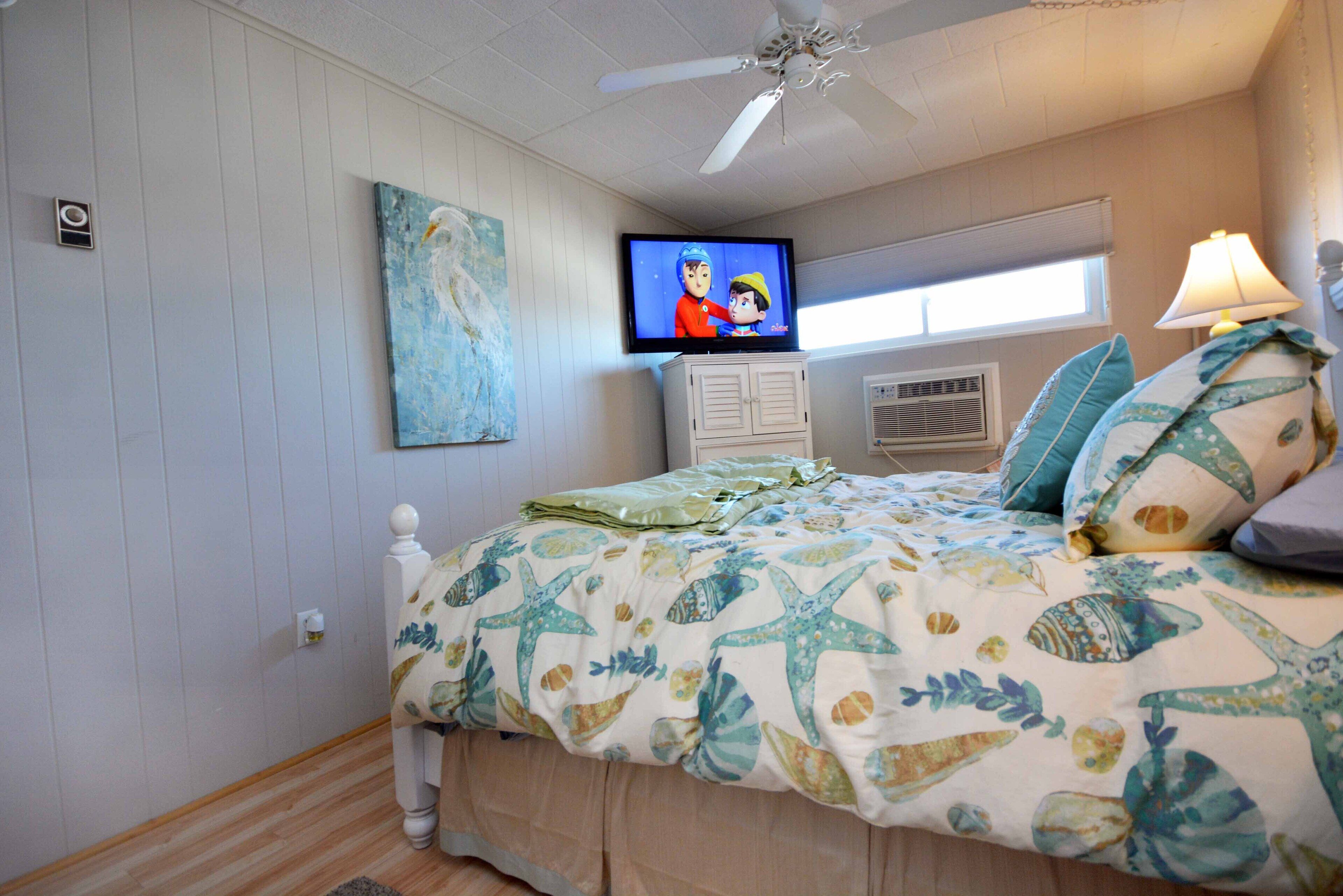 Een slaapkamer met een bed, een televisie, een plafondventilator en een raam.