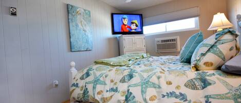 Een slaapkamer met een bed, een televisie, een plafondventilator en een raam.