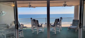 Un balcon avec des chaises blanches, une table et une vue sur l’océan.