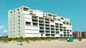 A multi-story hotel with a flat roof, located near a sandy beach. - Stylish, cozy 2 bedroom luxury oceanfront condo with free WiFi, an outdoor pool, and a stunning ocean view from a covered balcony and only steps from the beach in midtown! (Ocean City)