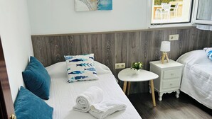A bedroom with two beds, a small table, a nightstand, and a window with a view of the outside. - Casa con Jardin en el Salnes (Meaño)
