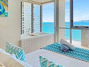 Une chambre d’hôtel avec un lit, une fenêtre donnant sur la mer et une salle de bain avec un lavabo, ainsi qu’une autre fenêtre donnant sur la mer.