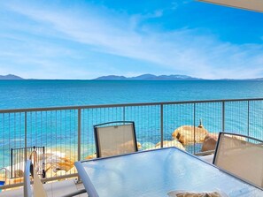 Un balcon avec une table et des chaises donnant sur une étendue d’eau et sur des montagnes lointaines.