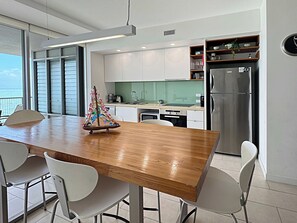 A modern kitchen with white cabinets, a stainless steel refrigerator, and a wooden dining table with chairs.