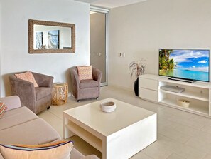Een moderne woonkamer met een flatscreen televisie, twee fauteuils, een bank, een salontafel en een decoratieve spiegel.