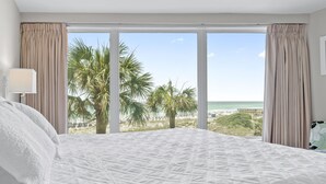 Ein Hotelzimmer mit einem großen Bett, Blick auf den Strand und Palmen.