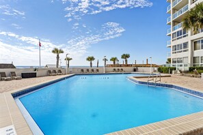 A swimming pool with lounge chairs, a wooden deck, and a view of the ocean.