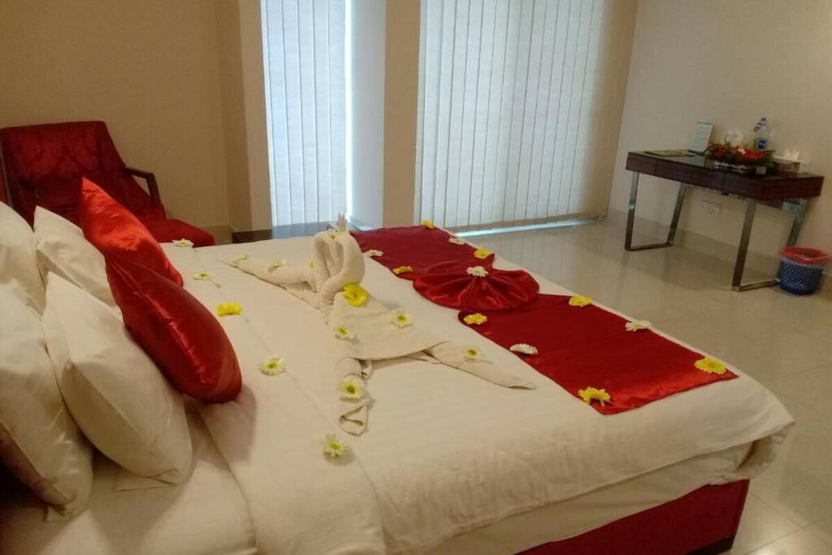 A neatly made bed with white and red linens, a red chair, and a small table with a flower arrangement.
