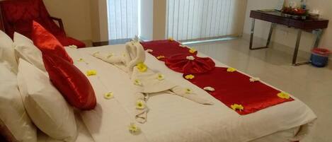 Un lit bien fait, avec du linge de lit blanc et rouge, une chaise rouge et une petite table agrémentée d’un arrangement floral.