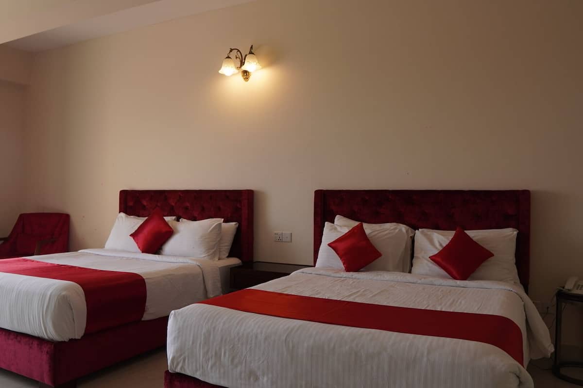 Two double beds with red headboards and white bedding, a red chair, and a wall-mounted light fixture.