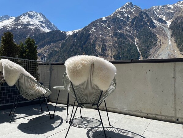 Two white chairs with fur throws on a balcony with a mountain view.