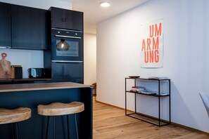Une cuisine moderne avec des meubles de couleur sombre, un four encastré et un coin bar en bois avec des tabourets.
