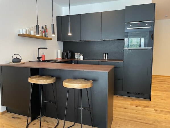 Une cuisine moderne avec des meubles de rangement aux couleurs sombres, un îlot central en bois doté de tabourets et un four encastré.