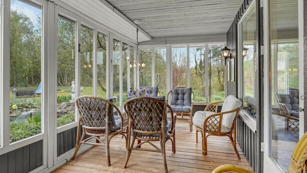 A covered porch with wicker chairs, a table with flowers, and a view of a garden. - 3 bedroom amazing home in Oksbøl (Oksbøl)
