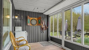 A covered porch with a dartboard, darts, and a dartboard stand. There is a wicker chair and a small table with a cushion. - 3 bedroom amazing home in Oksbøl (Oksbøl)